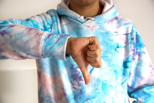 A person wearing a colorful tie-dye hoodie showing a thumbs down gesture, symbolizing disapproval.